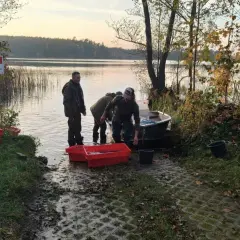Ludzie wyładowują ryby z łodzi do czerwonych pojemników nad jeziorem.