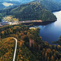 Malownicze jezioro Bystrzyckie otoczone jesiennymi lasami. Widok z lotu ptaka na spokojną taflę wody i zalesione wzgórza.