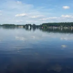 Spokojne **jezioro Pławniowice** z odbijającymi się chmurami i żaglówkami na horyzoncie.