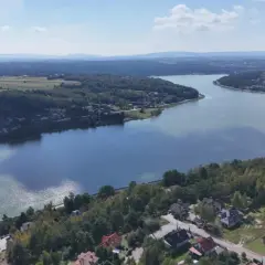 Widok z lotu ptaka na zalew Brody, otoczony lasami i domami. Widać tamę i fragment torów kolejowych.