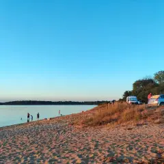 Piękny dzień nad **dzierżno duże**. Ludzie kąpią się w jeziorze, a na plaży stoją samochody i kampery.