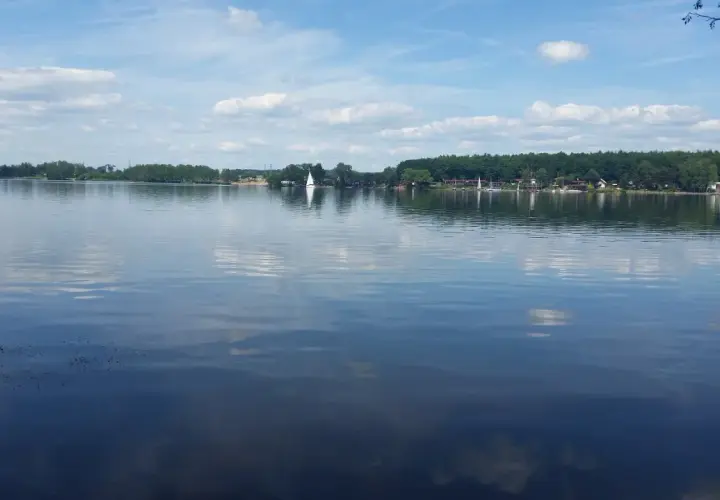 Spokojne **jezioro Pławniowice** z odbijającymi się chmurami i żaglówkami na horyzoncie.