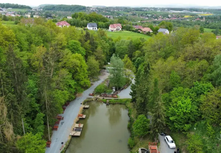 Widok z lotu ptaka na łowisko pstrągowe otoczone zielonymi drzewami, z domami w tle.
