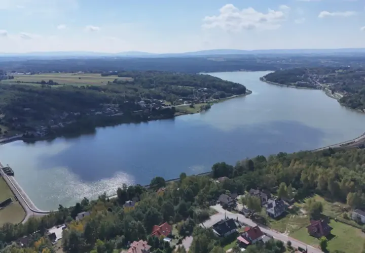 Widok z lotu ptaka na zalew Brody, otoczony lasami i domami. Widać tamę i fragment torów kolejowych.