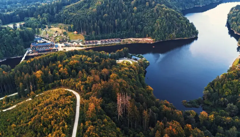 Malownicze jezioro Bystrzyckie otoczone jesiennymi lasami. Widok z lotu ptaka na spokojną taflę wody i zalesione wzgórza.