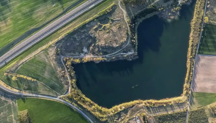 Widok z lotu ptaka na jezioro otoczone polami i drogą.