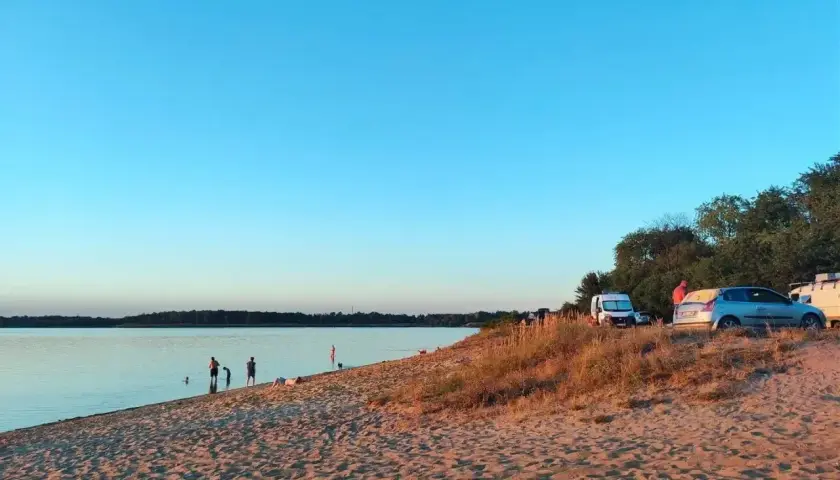 Piękny dzień nad **dzierżno duże**. Ludzie kąpią się w jeziorze, a na plaży stoją samochody i kampery.