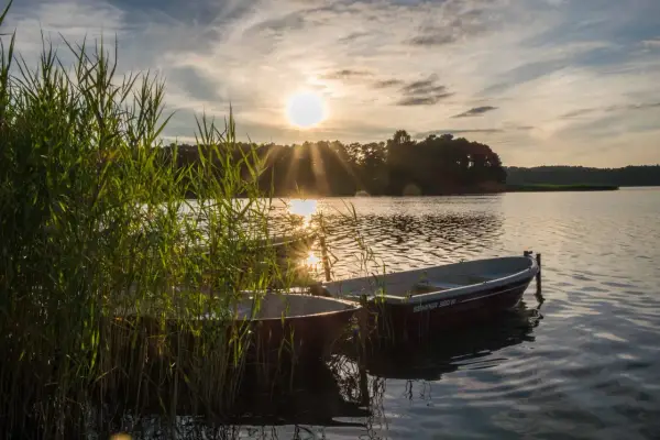 Dwa łodzie kołyszą się na falach jeziora Świętajno. Słońce zachodzi, rzucając złote promienie na wodę i trzciny.