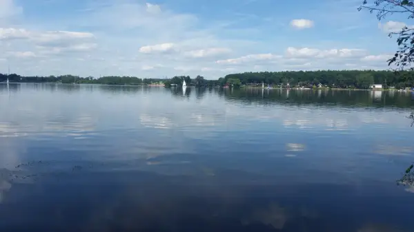 Spokojne **jezioro Pławniowice** z odbijającymi się chmurami i żaglówkami na horyzoncie.
